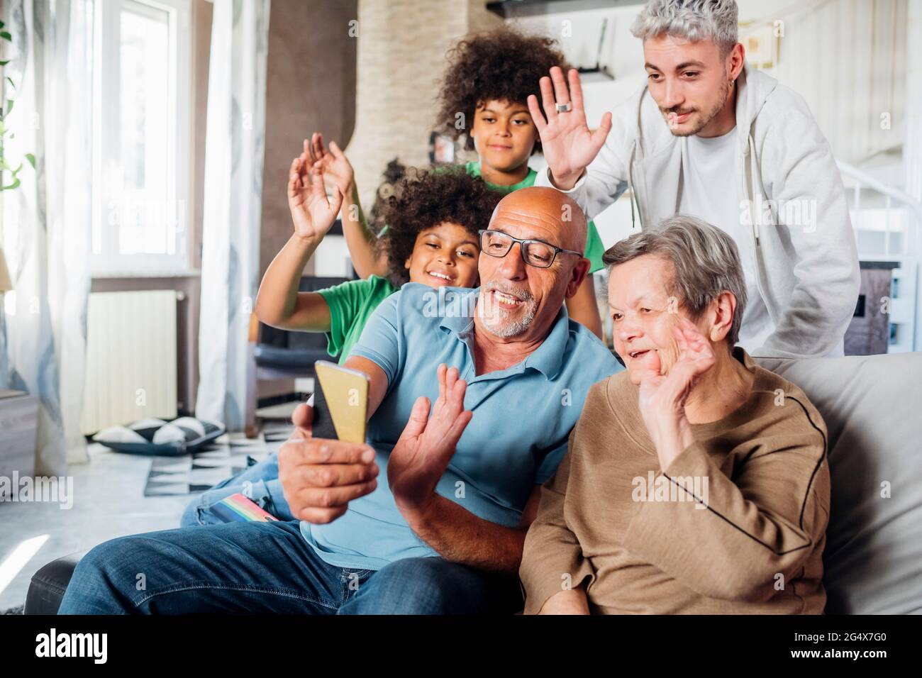 Multiethnic family waving hands together while doing video call through smart phone at home Stock Photo