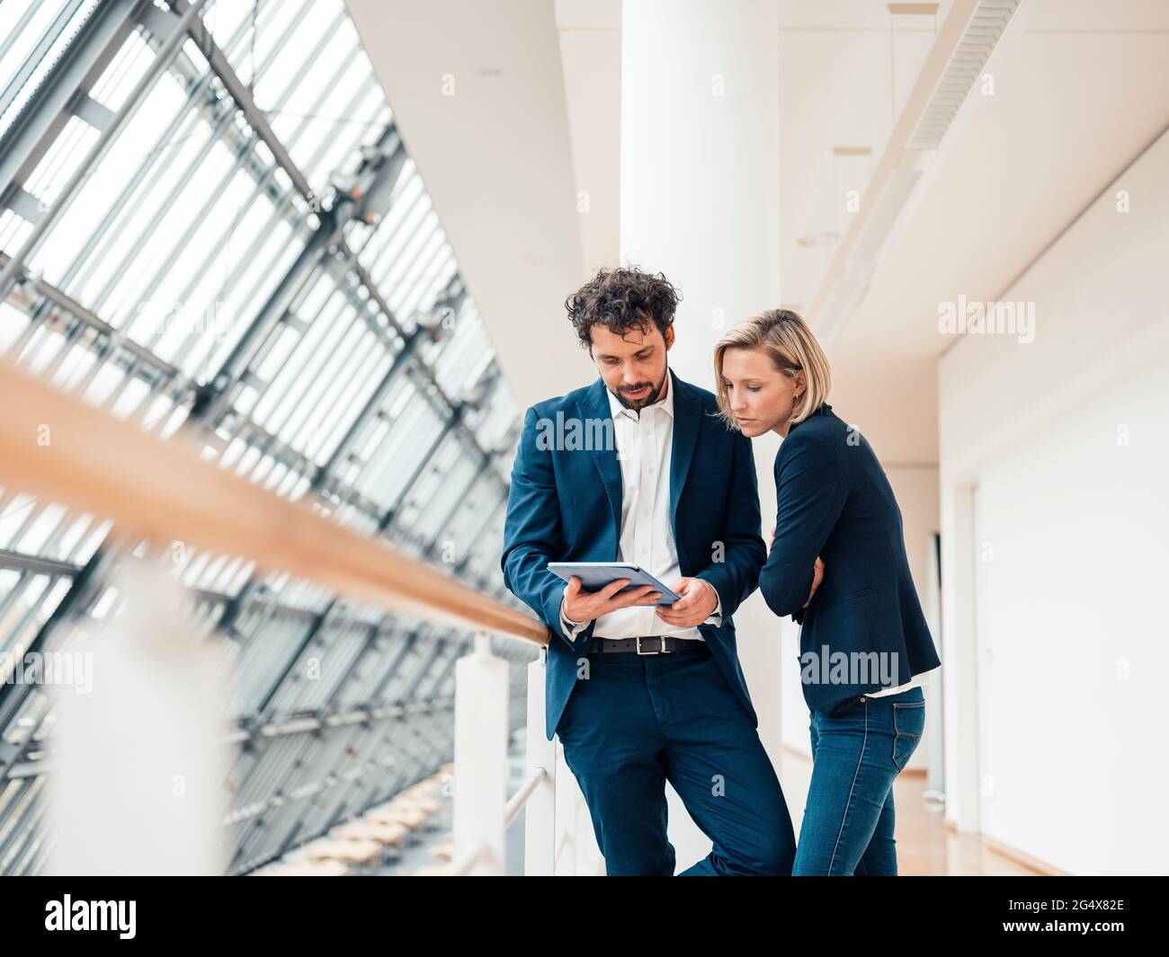 Professional team using digital tablet while standing at office corridor Stock Photo