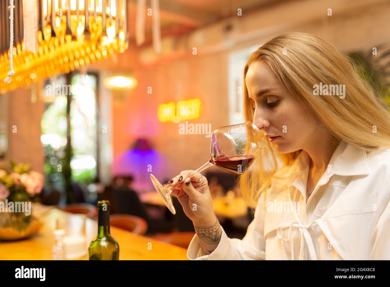 Young blond woman drinking red wine while sitting at bar Stock Photo