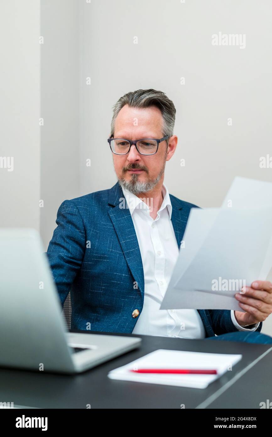 Businessman with document using laptop while working at office Stock Photo
