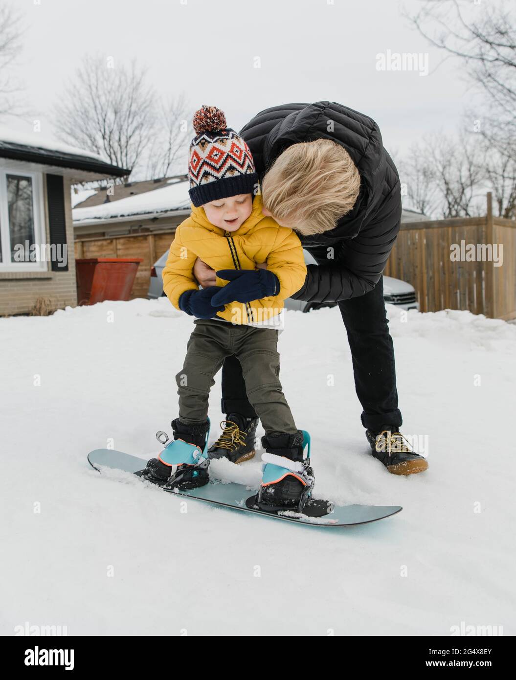 Loving father embracing son learning snowboarding during winter Stock Photo