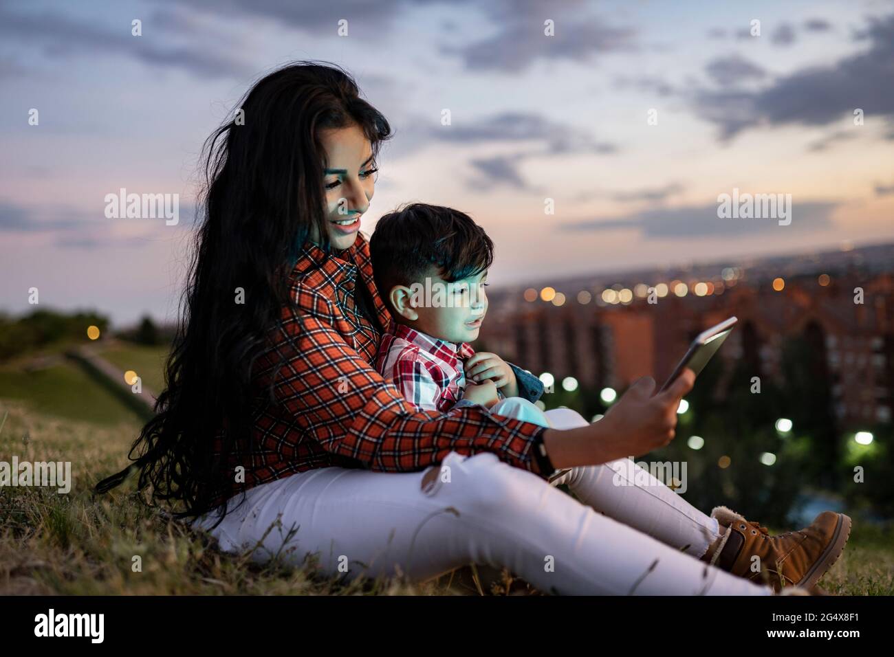 Mother using digital tablet while sitting with son on hill Stock Photo