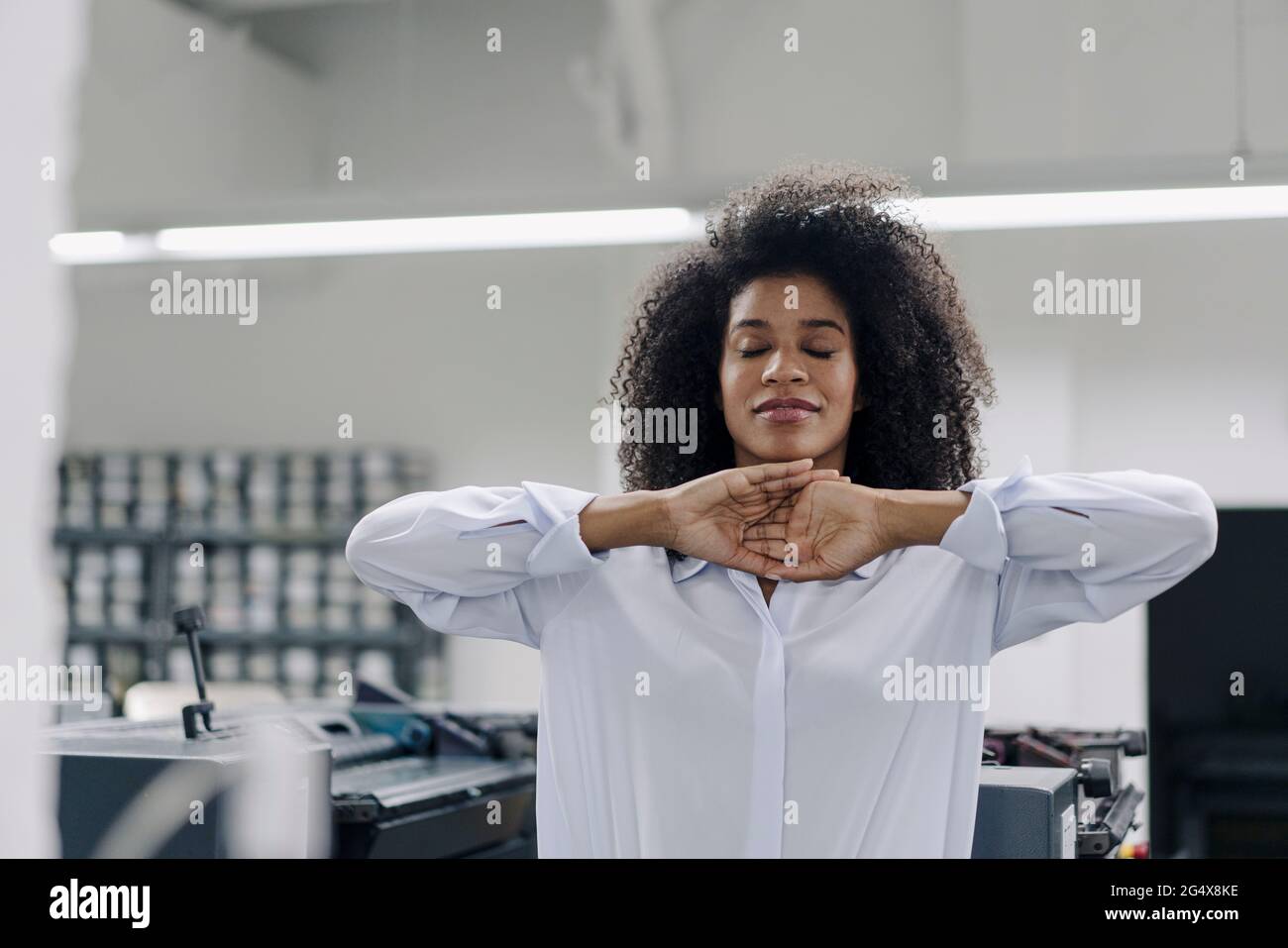 Businesswoman with hands clasped practicing relaxation exercise at industry Stock Photo