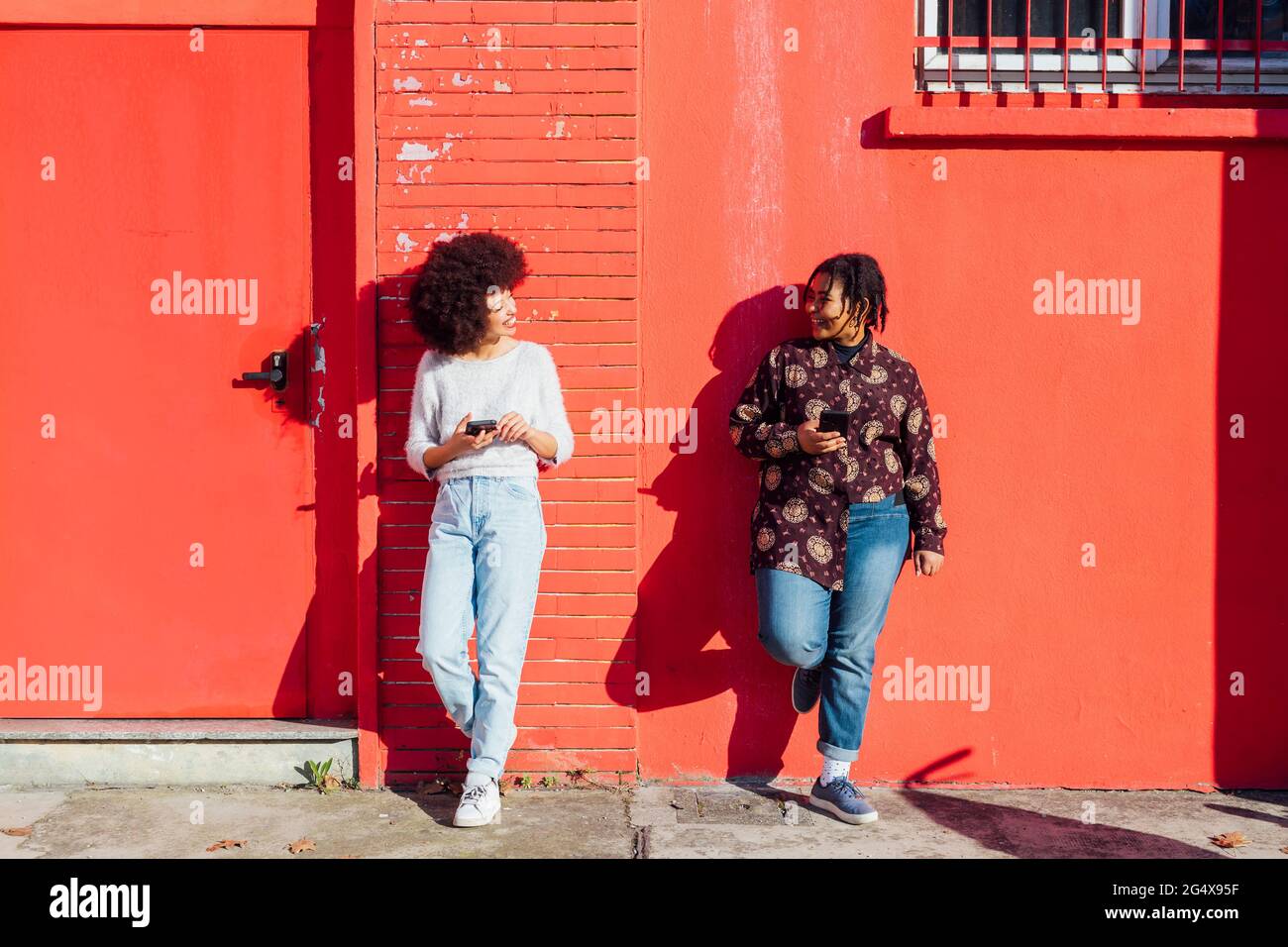 Multi-ethnic friends talking while leaning on red building Stock Photo