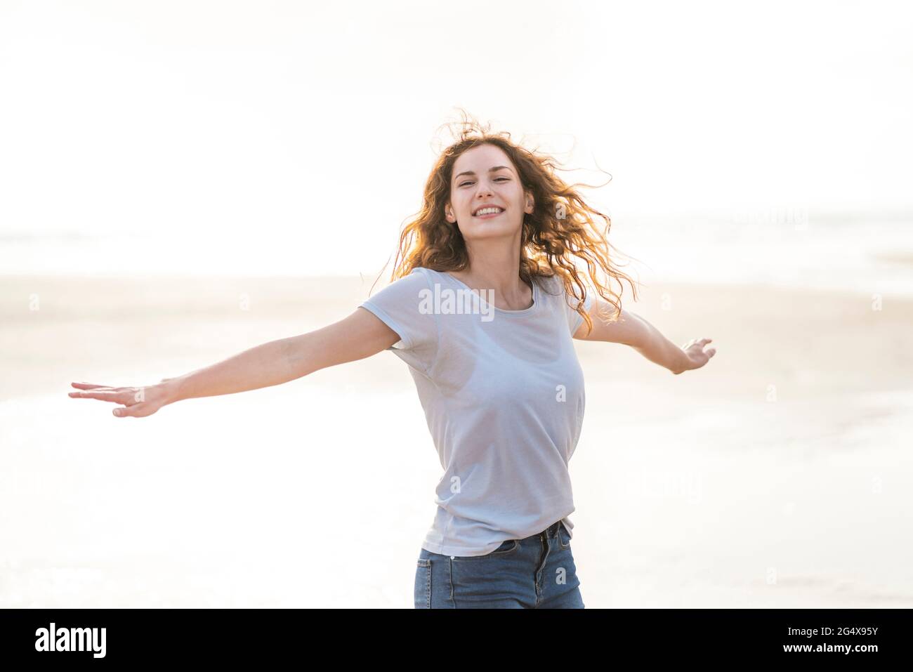 Carefree woman with arms outstretched spinning around at beach Stock