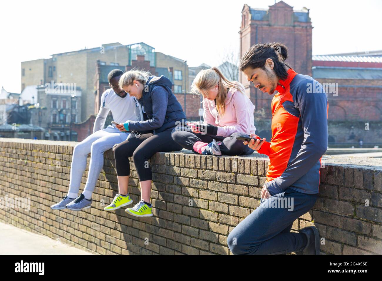 Multi-ethnic fitness friends using smart phones at wall Stock Photo