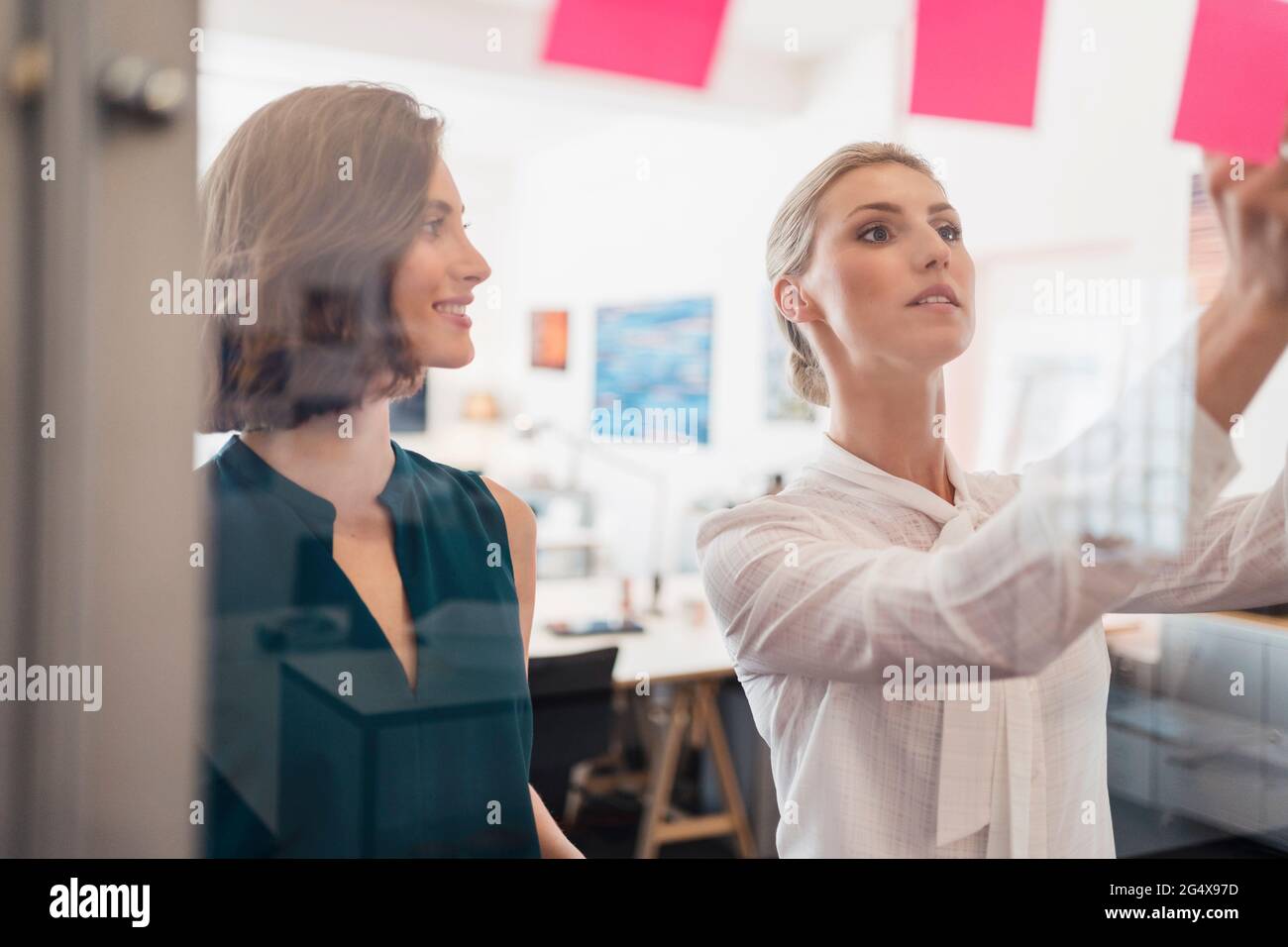 Smiling businesswoman looking at female colleague working in office seem through glass Stock Photo