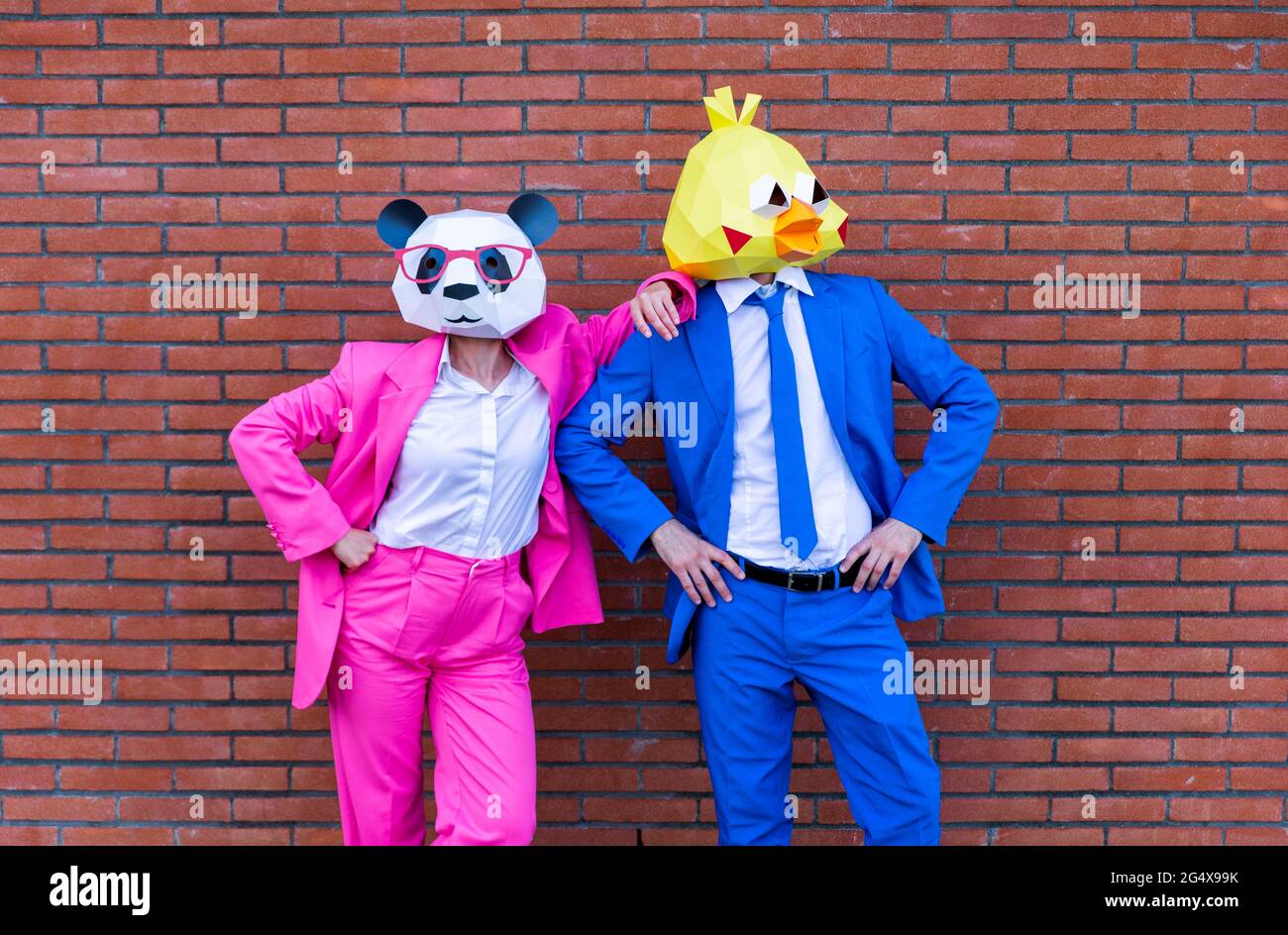 Man and woman wearing vibrant suits and animal masks posing together in