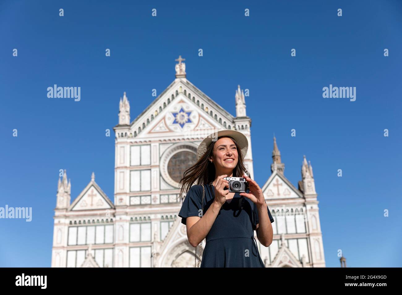 Smiling female tourist standing with camera in front of Basilica Of Santa Croce, Florence, Italy Stock Photo