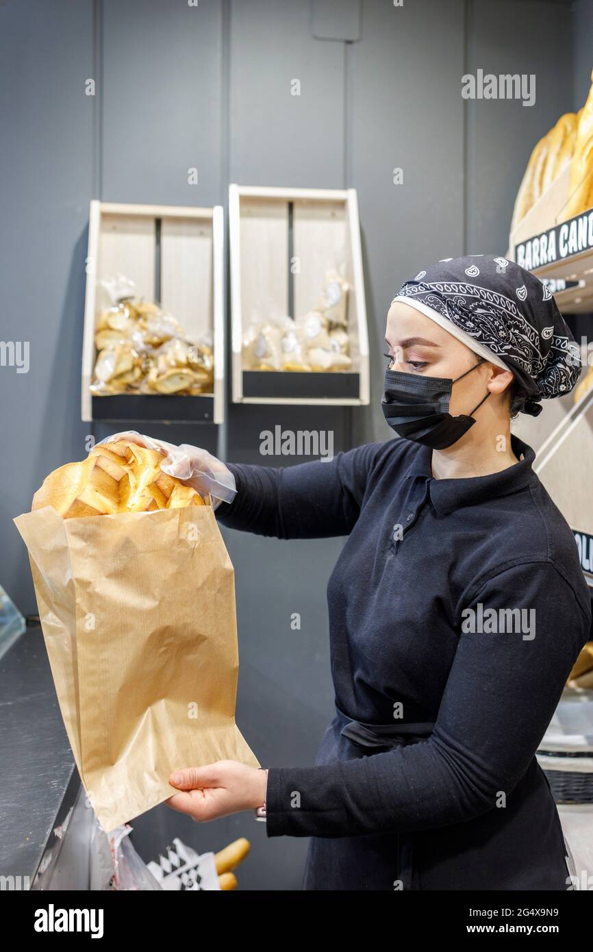 Female baker packing pastry item in paper bag at bakery Stock Photo