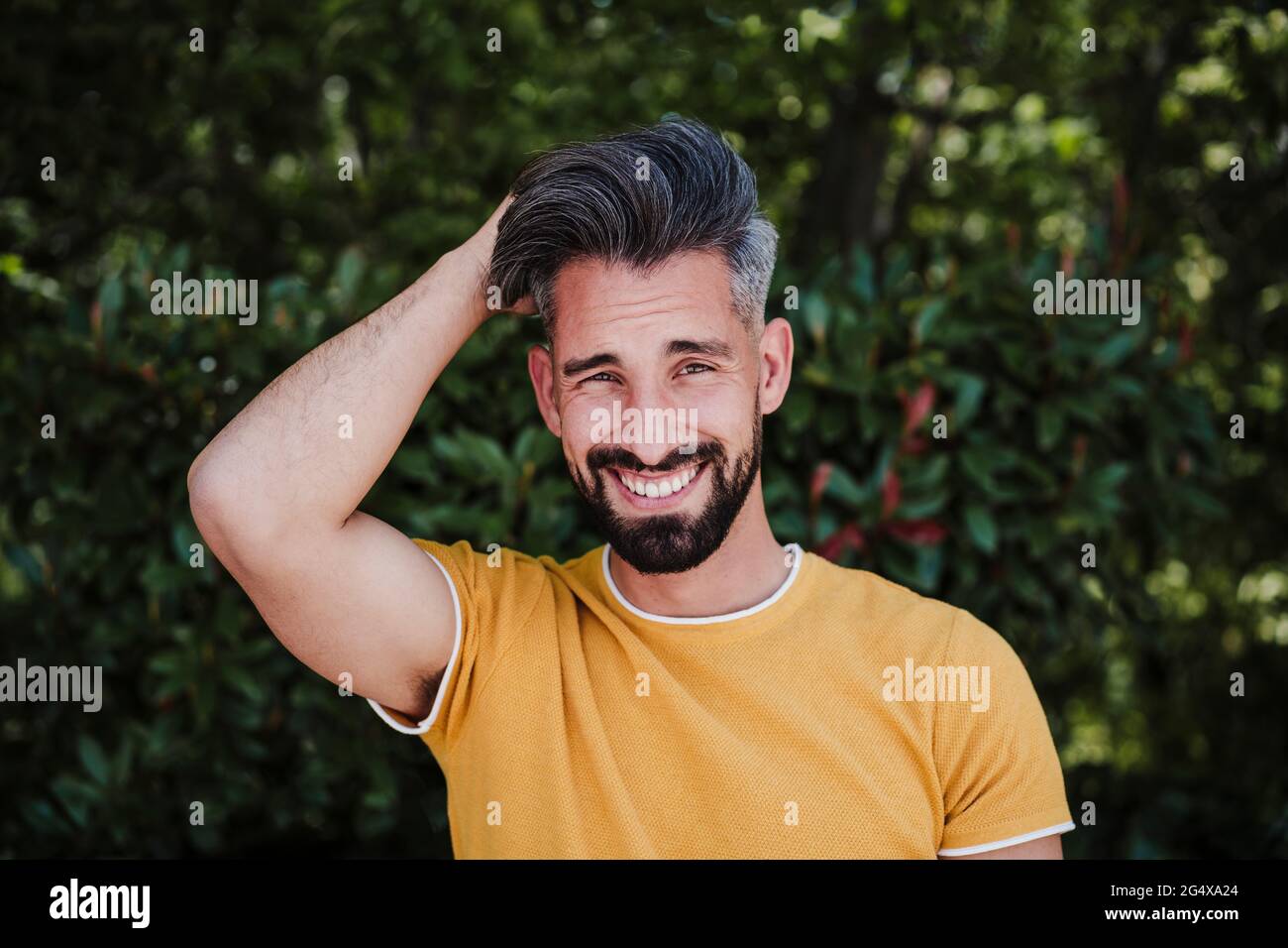 Smiling bearded man with hand in hair at park Stock Photo