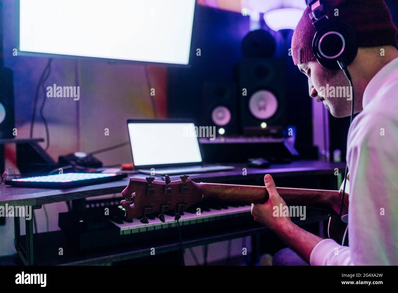 Man wearing headphones playing guitar at home studio Stock Photo