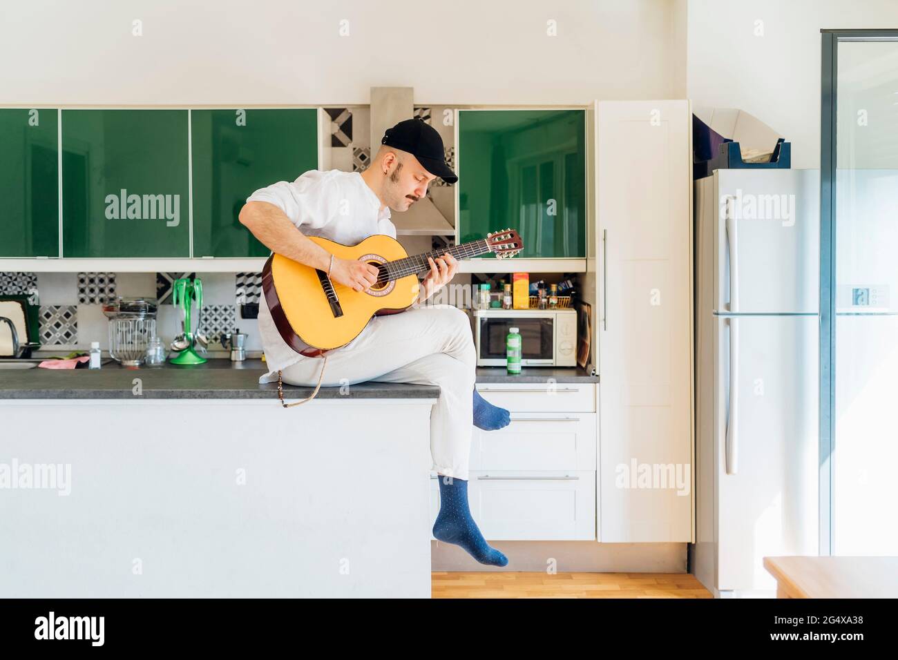 Male composer with eyes closed playing guitar on kitchen island at home Stock Photo