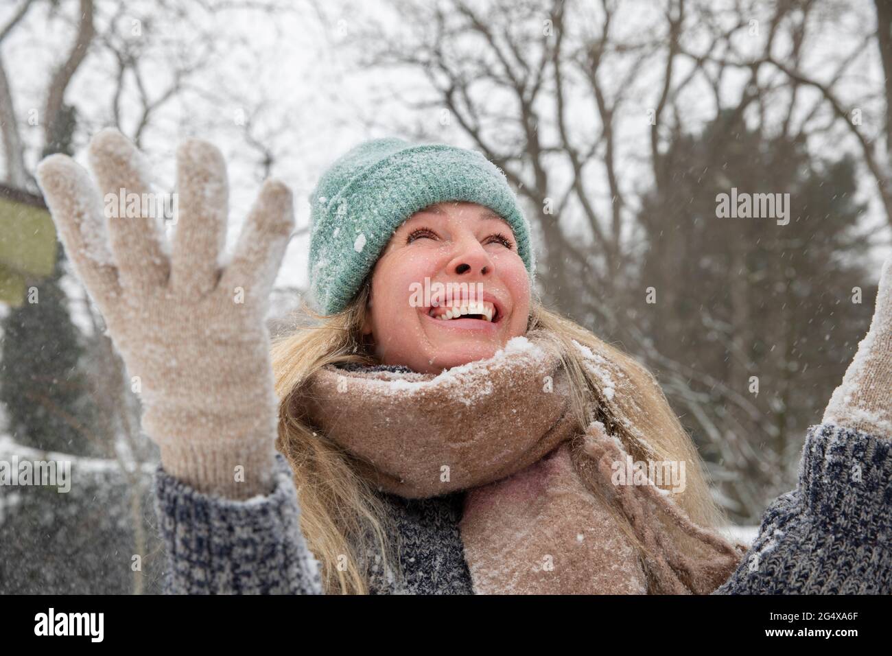Cheerful blond woman throwing snowing while playing during winter Stock Photo