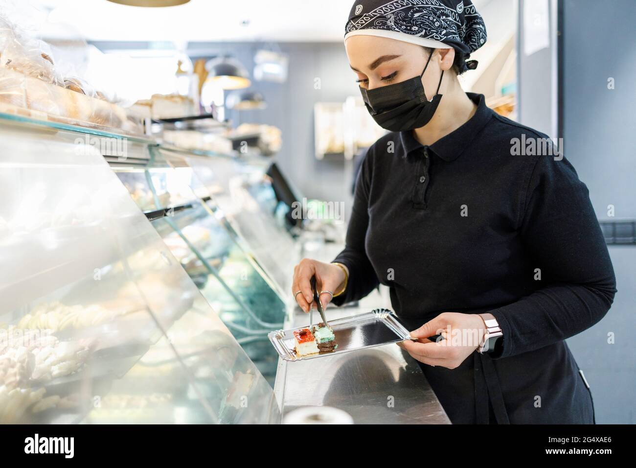 Female owner with cake on tray at display cabinet in bakery Stock Photo