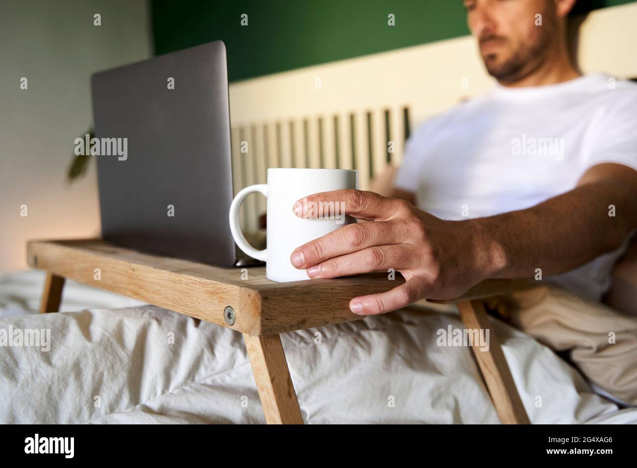 Man working on laptop while sitting in bed at home Stock Photo