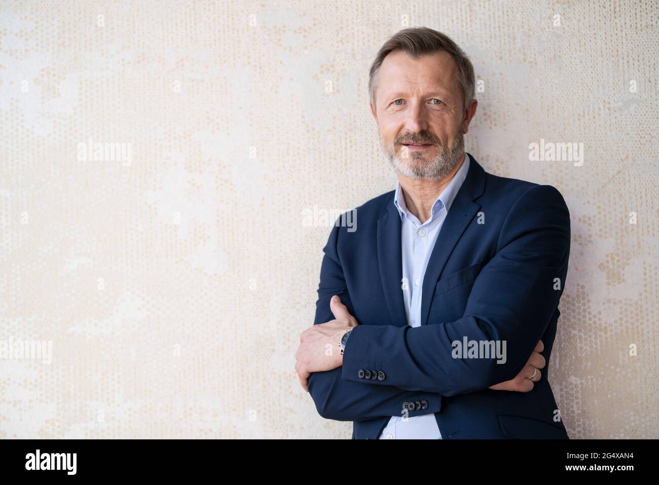 Confident male entrepreneur standing with arms crossed in front of wall ...