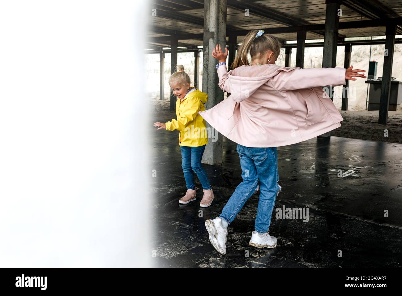Sisters wearing raincoats playing under roof at cafe Stock Photo Alamy
