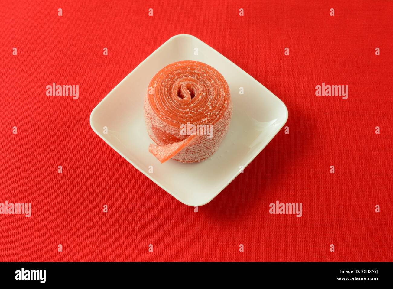 Sour strawberry fruit roll up candy in white candy dish on red background Stock Photo