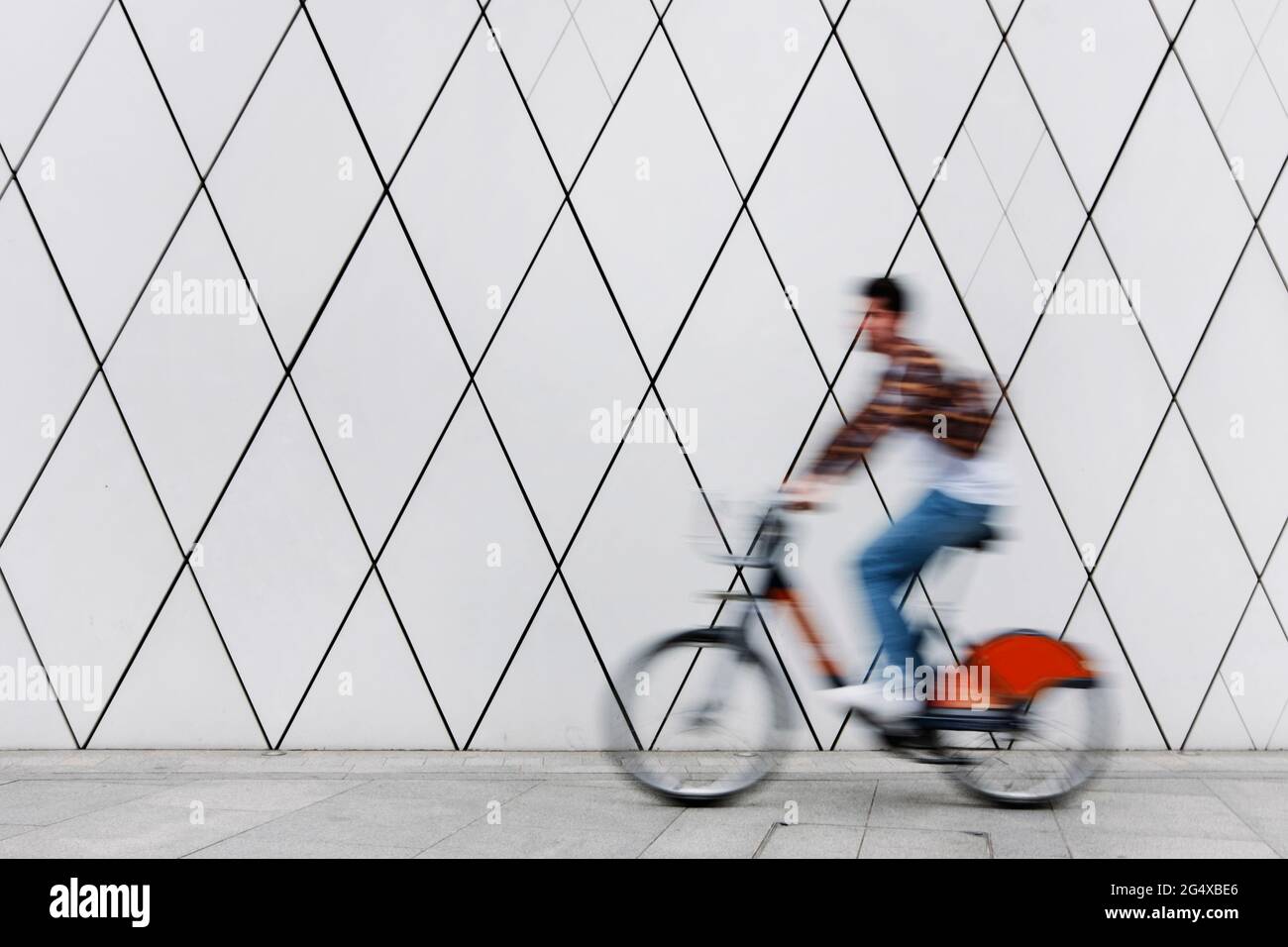 Young man cycling on footpath by wall Stock Photo