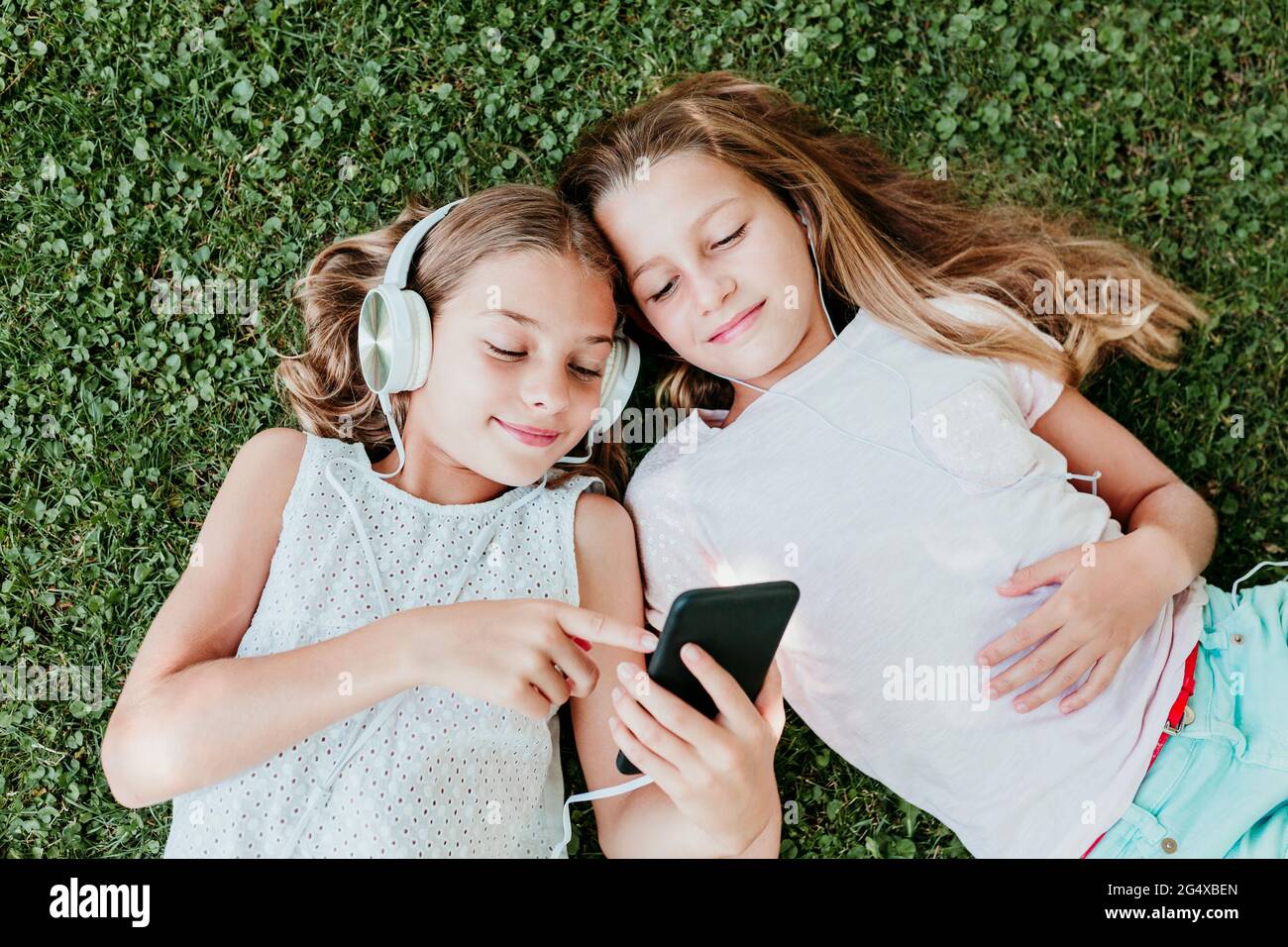 Smiling friends listening music while lying on grass in summer Stock Photo