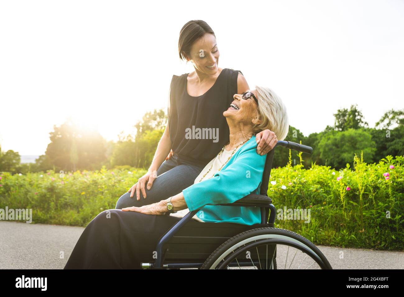 Granddaughter smiling while looking at grandmother sitting in wheelchair Stock Photo