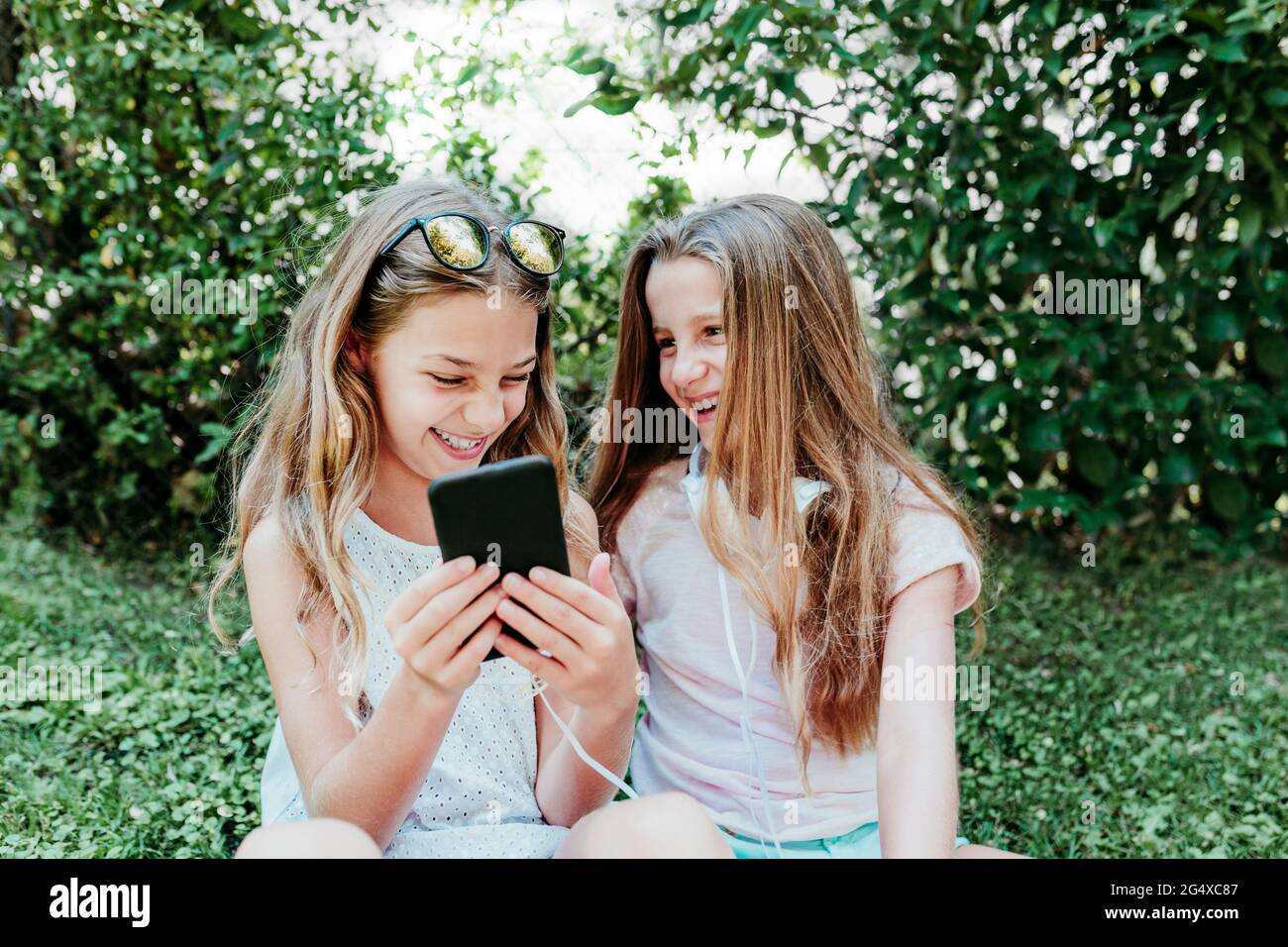 Cheerful girl with friend using mobile phone in garden Stock Photo