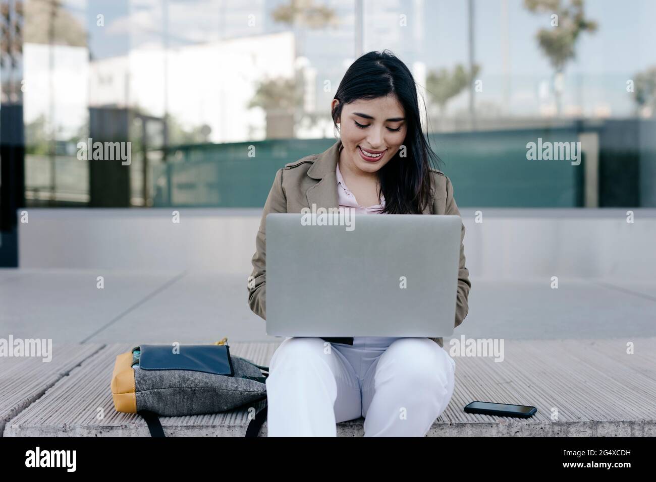 Smiling female freelancer using laptop while sitting on footpath Stock Photo