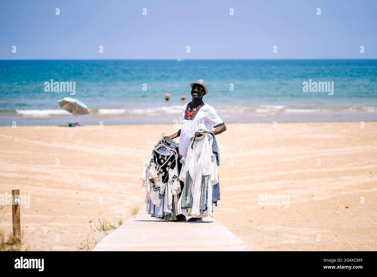 Male vendor standing on boardwalk while selling clothes at beach during sunny day Stock Photo