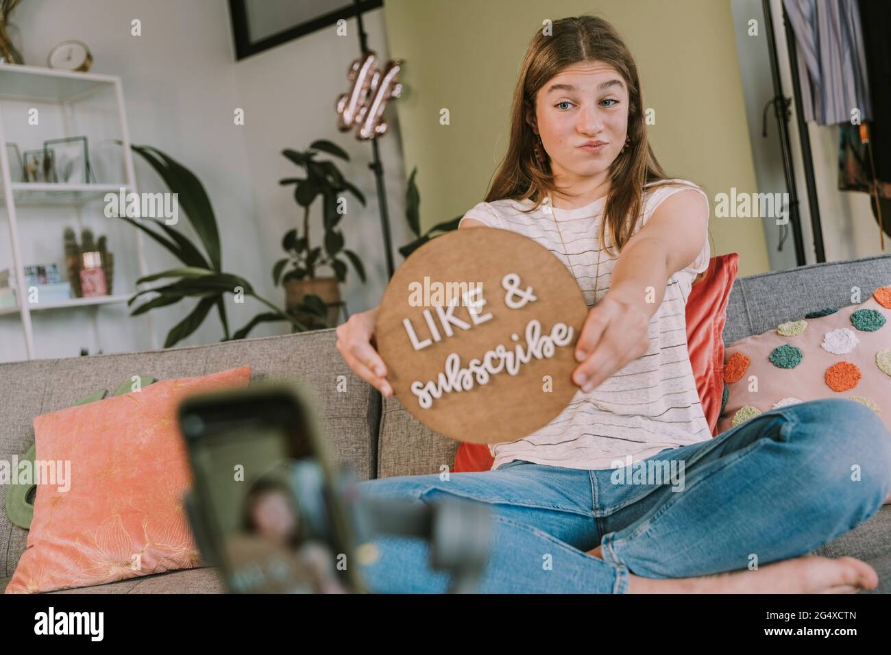 Girl holding like and subscribe sign while filming at home Stock Photo