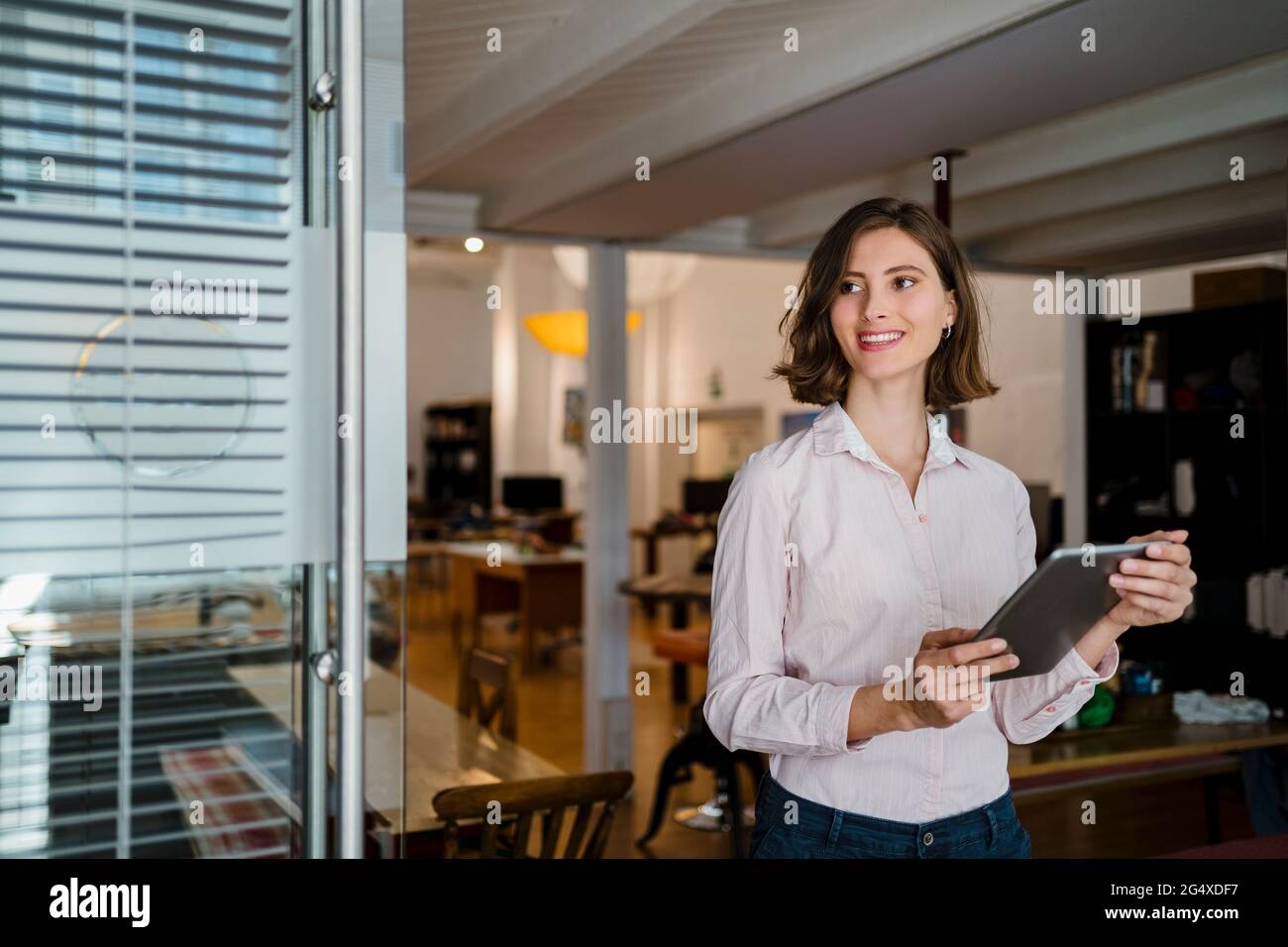 Smiling young female professional wit digital tablet standing in office while looking away Stock Photo