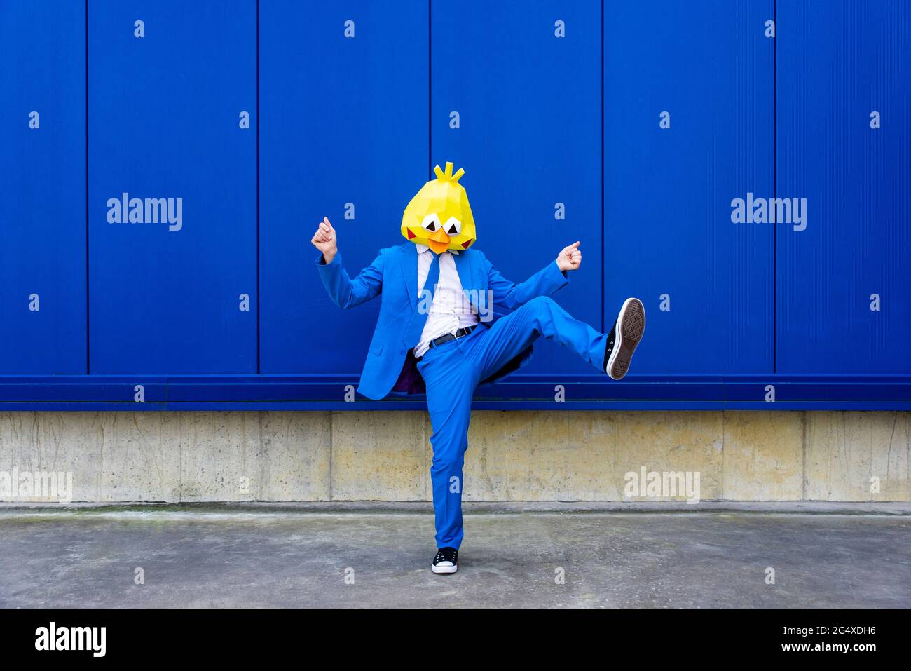 Man wearing vibrant blue suit and bird mask standing on one leg against