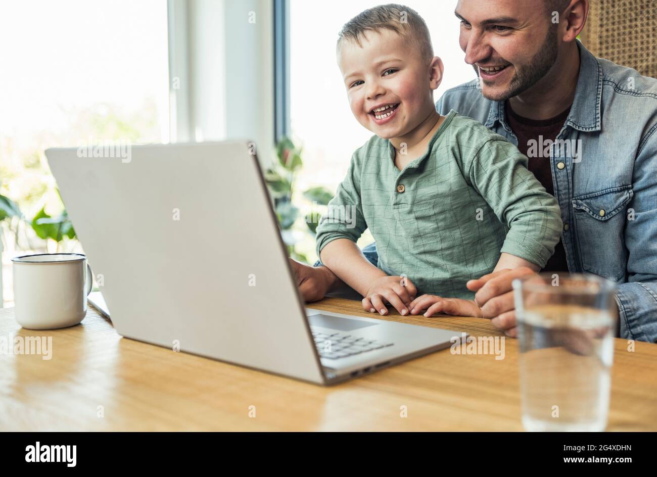 Cheerful son and father sitting with laptop doing video call at home Stock Photo