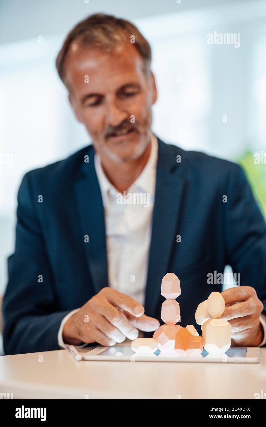 Male entrepreneur stacking wooden rock on digital tablet in office Stock Photo