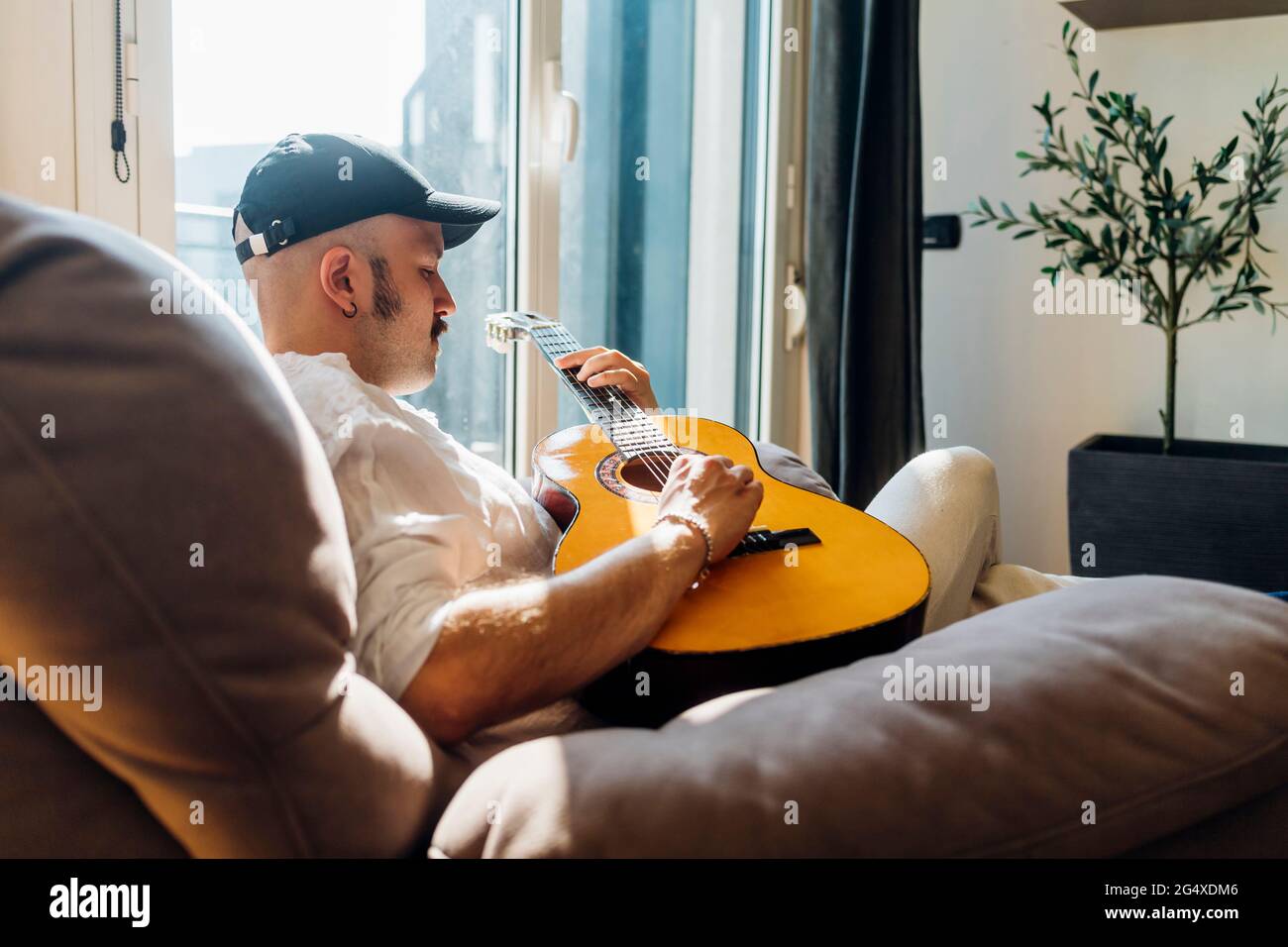 Male composer playing guitar while sitting on reclining chair at home Stock Photo
