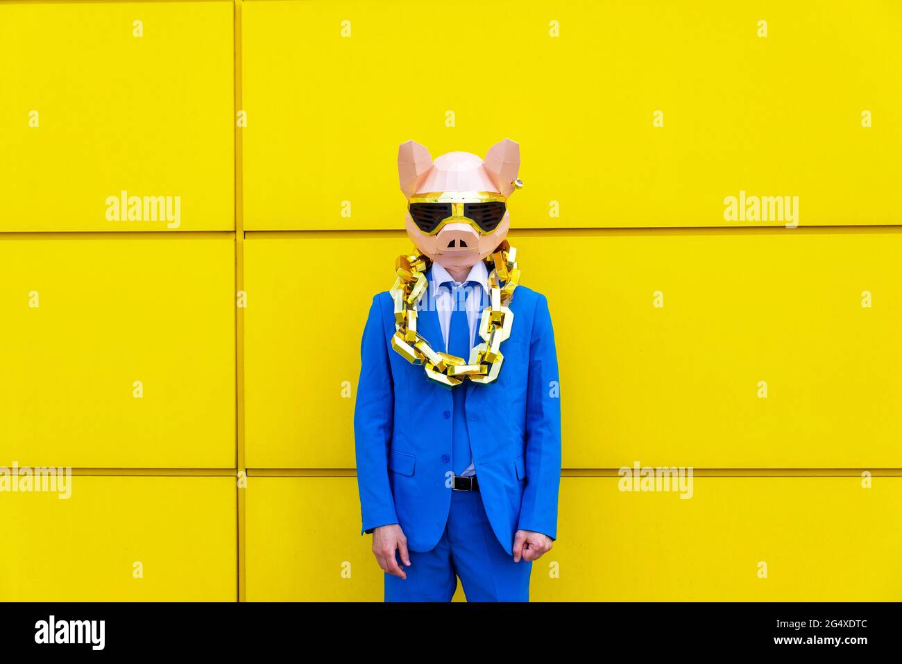 Man wearing vibrant blue suit, pig mask and large golden chain standing