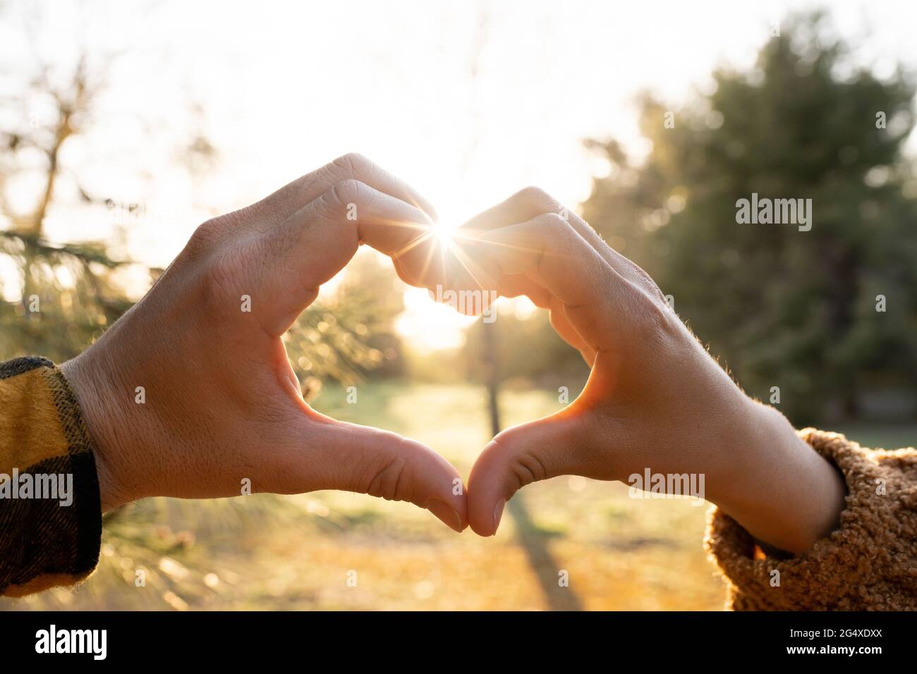 Man and woman's hands making heart shape symbol during sunset Stock Photo