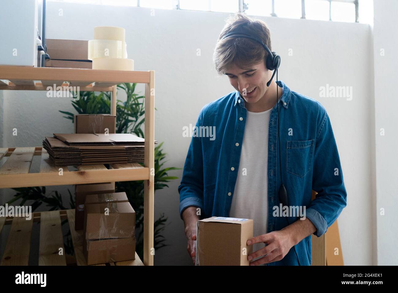 Smiling male customer service representative looking at box by rack in warehouse Stock Photo