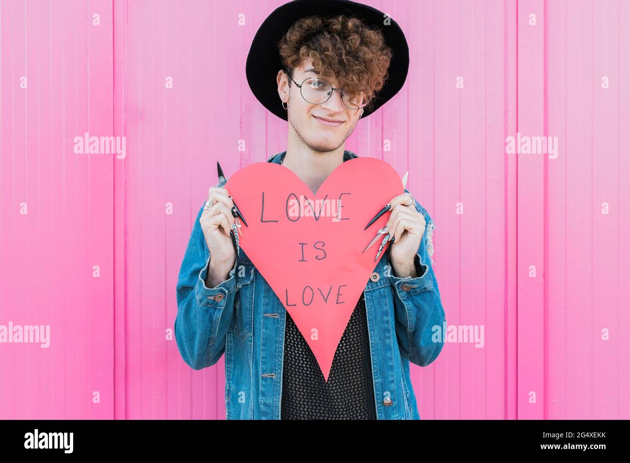 Smiling man with heart shape paper standing in front of pink wall Stock Photo