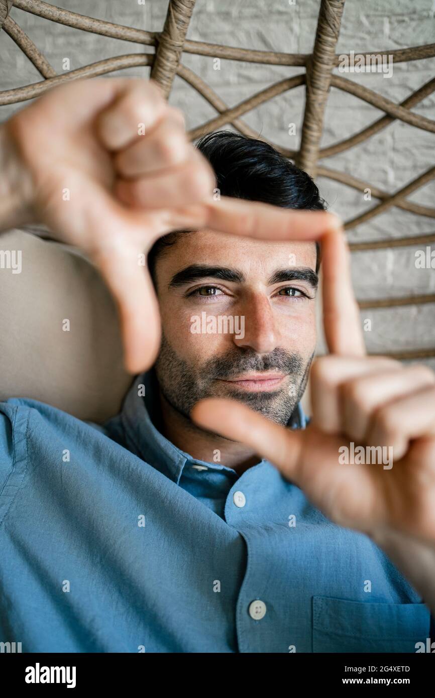 Man making finger frame while sitting on chair swing Stock Photo