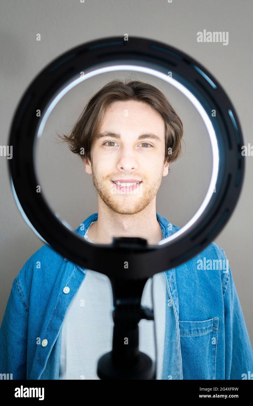 Smiling man standing in front of illuminated ring light Stock Photo Alamy