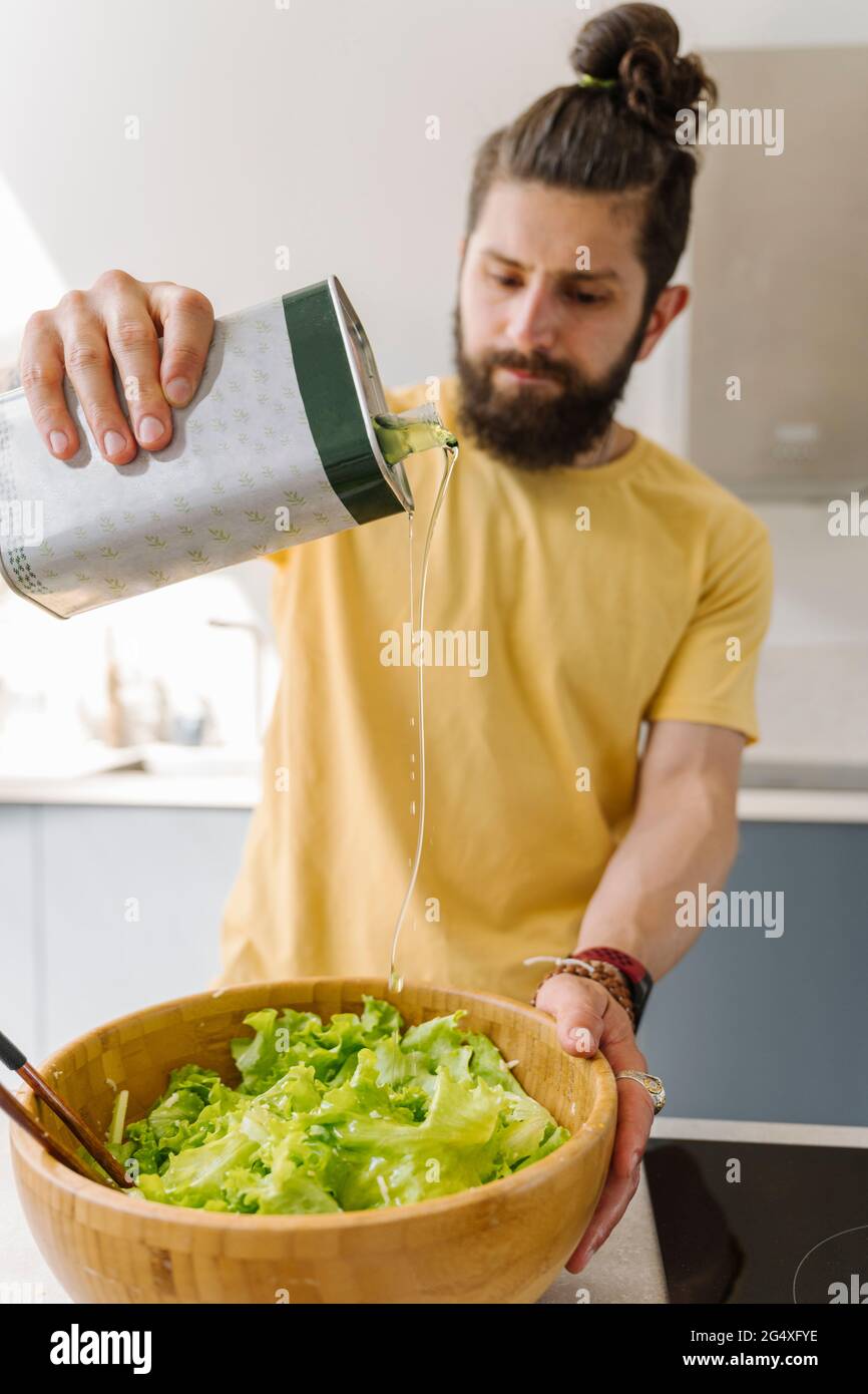 Man putting olive oil in salad bowl at home Stock Photo