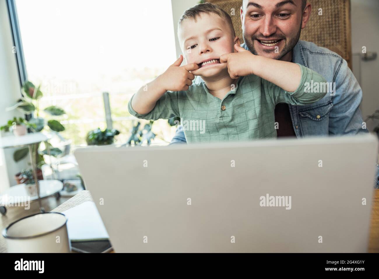 Boy teasing while sitting with father doing video call through laptop at home Stock Photo