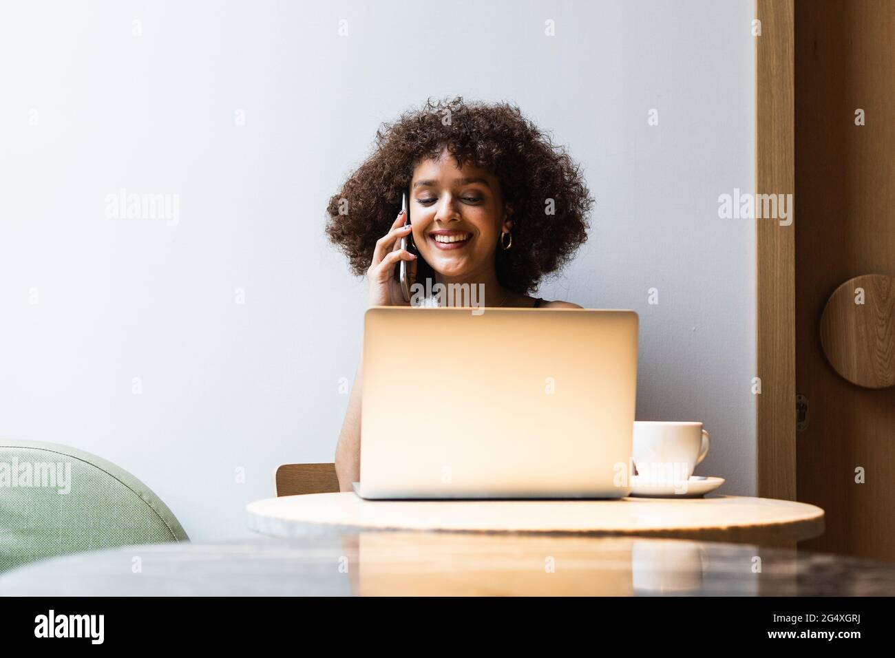 Female university student talking on mobile phone while sitting at cafe Stock Photo