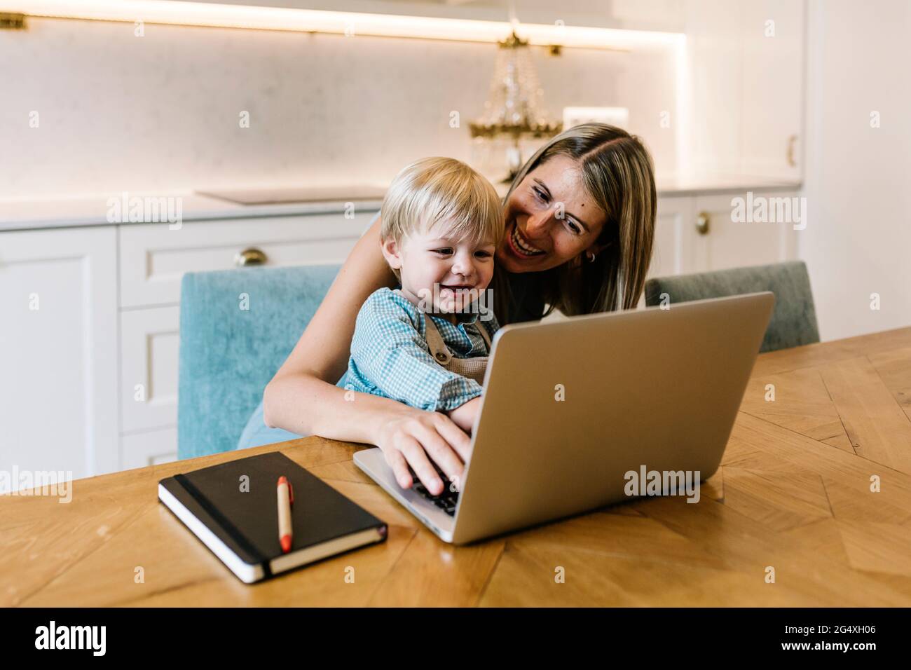 Smiling boy using laptop with mother working at home Stock Photo