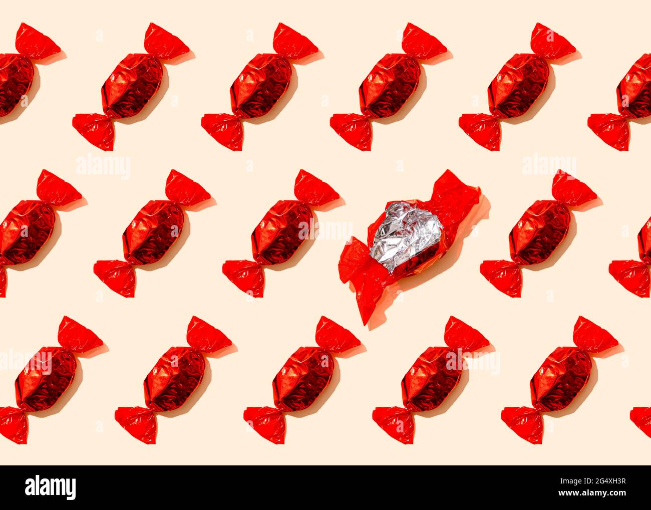 Pattern of rows of red wrapped candies with single empty wrapper Stock Photo