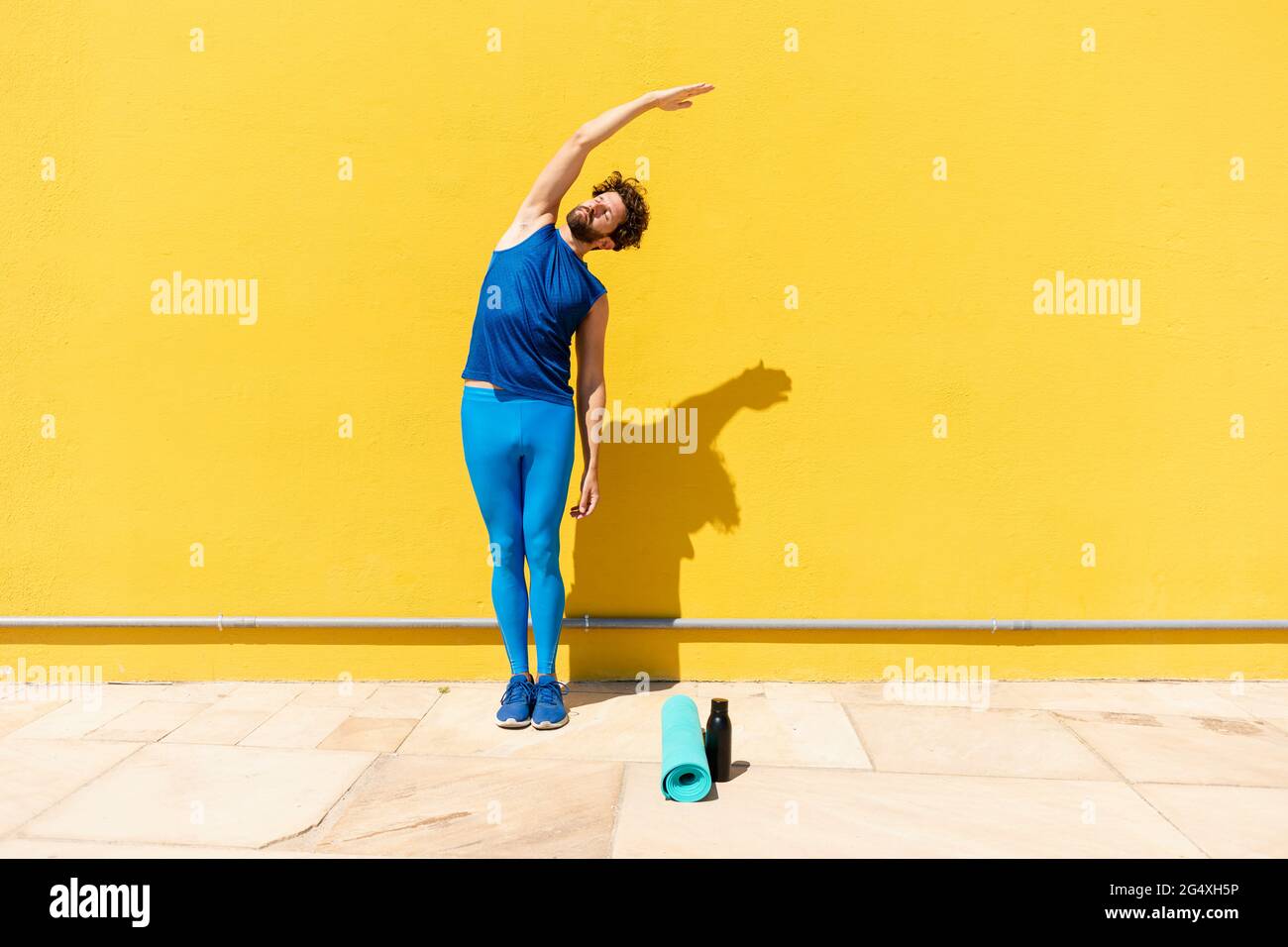 Man doing stretching exercise while standing in front of yellow wall Stock Photo
