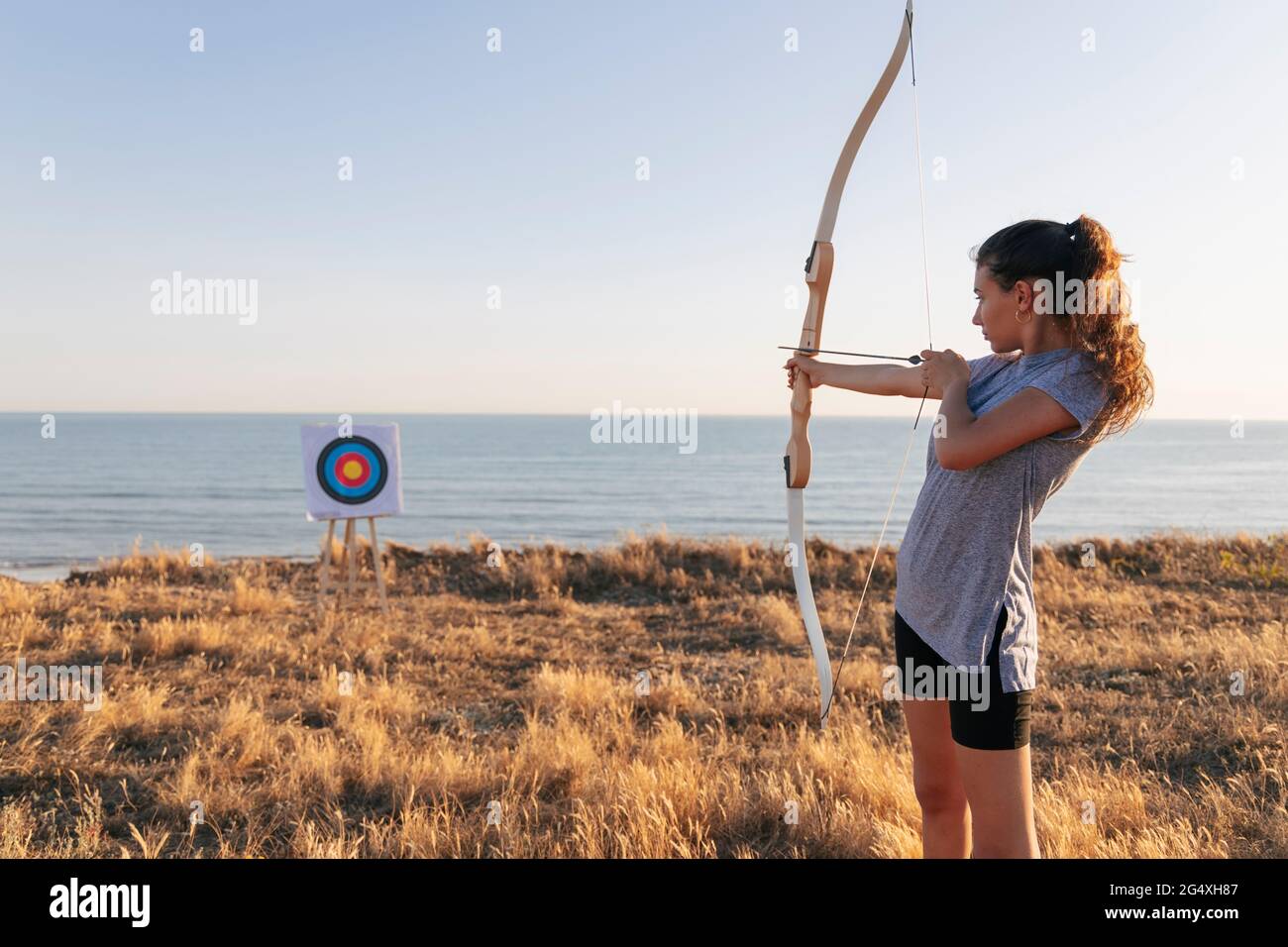 Archeress aiming at target while standing on grass during sunny day Stock Photo