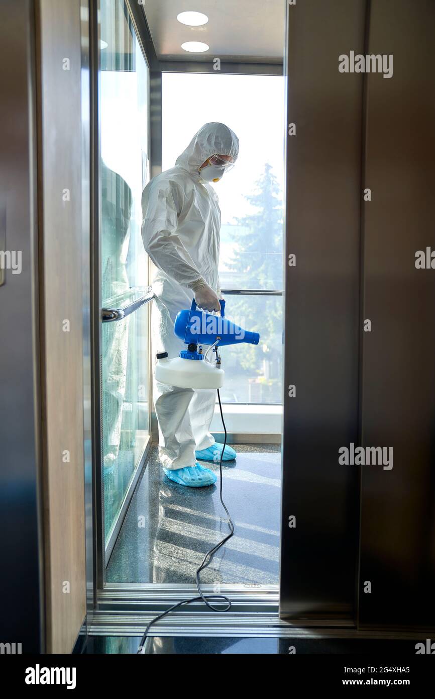 Female frontline worker using disinfection in office elevator Stock Photo
