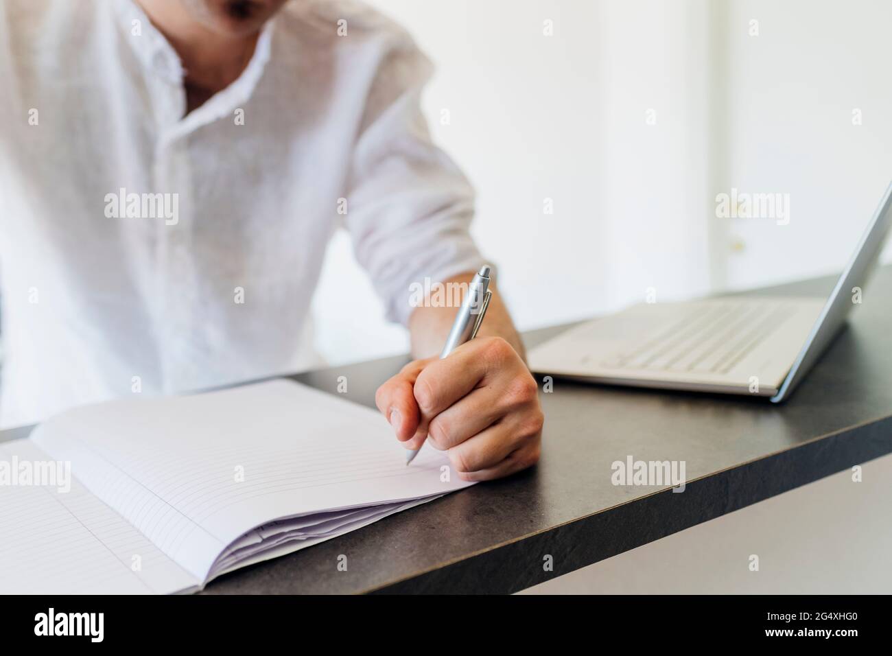 Man making list on book by laptop at kitchen island Stock Photo